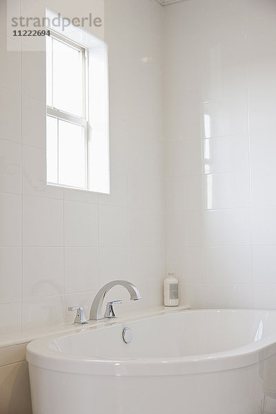 Nahaufnahme einer weißen Badewanne mit gefliester Wand und Fenster im Badezimmer