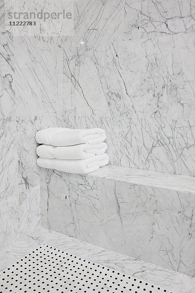 Gefaltete weiße Handtücher auf einem Marmorsitz im heimischen Badezimmer