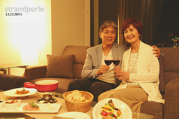 Modisches japanisches Seniorenpaar stößt auf dem Sofa an