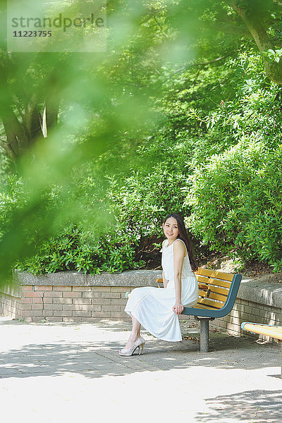 Junge japanische Frau sitzt auf einer Bank in einem Stadtpark