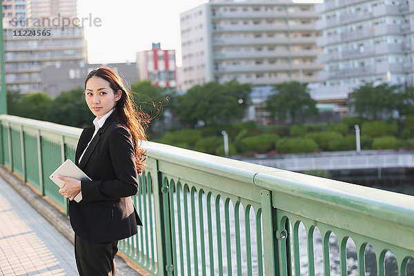 Porträt einer jungen japanischen Geschäftsfrau an einem Fluss in der Innenstadt von Tokio