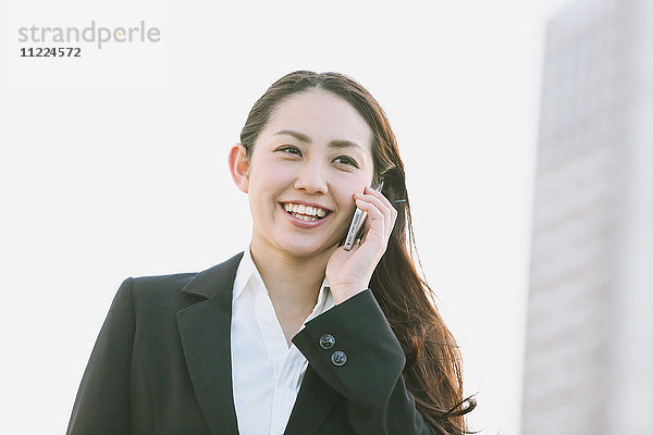 Junge japanische Geschäftsfrau am Telefon an einem Fluss in der Innenstadt von Tokio