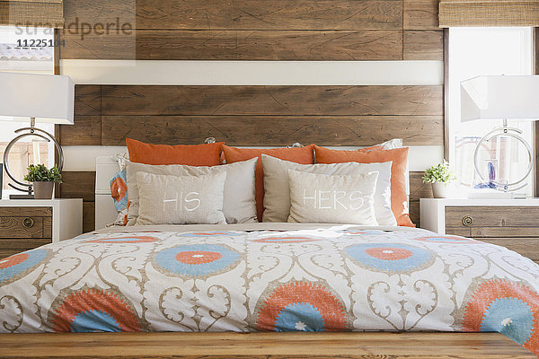 Gemütliches und aufgeräumtes Bett mit holzgetäfelter Wand in einem modernen Schlafzimmer
