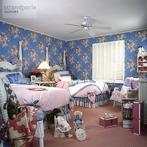 Doppelstockbetten für Mädchen  blaue und rosa geblümte Wände. Rosa Vorleger. Weiße Holzfensterläden am Fenster. Puppen.