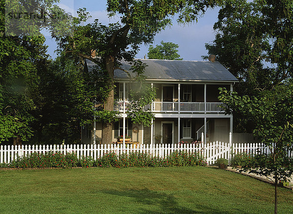 Zweistöckiges Haus  weißer Lattenzaun  Veranden auf beiden Ebenen über die gesamte Länge des Hauses