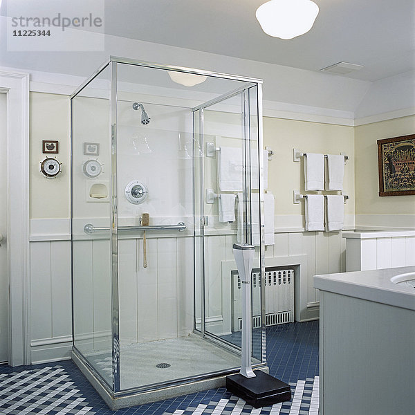 Blick auf eine Duschkabine mit Glaskasten  blaugrüner und weißer Fliesenboden  Waage  weiße Handtücher.
