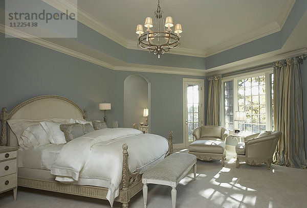 Zartblaue Wände  weiße Holzverkleidung  französischer Stil  weiße Bettwäsche  hell gebeizte Möbel  Kronleuchter  Sitzecke vor dem Fenster  gestreifte Vorhänge