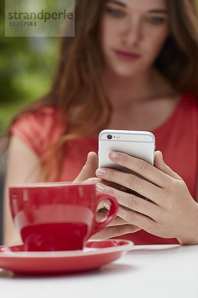 Frau benutzt Smartphone mit Kaffee