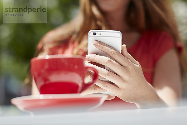 Frau benutzt Smartphone mit Kaffee