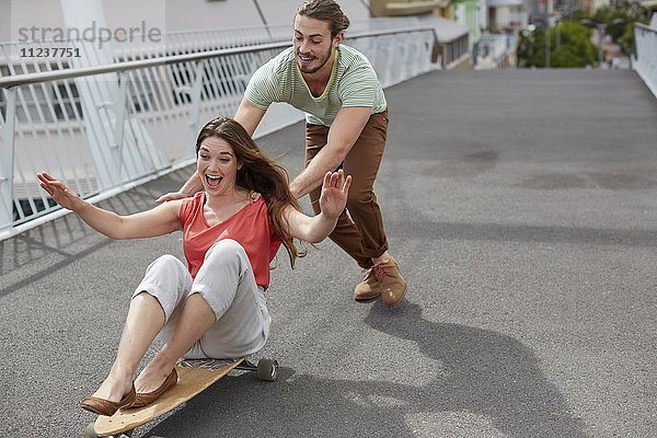 Frau auf Skateboard  Mann schiebend