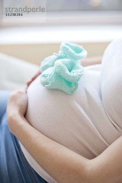 Schwangere Frau mit Babyschuhen auf dem Bauch