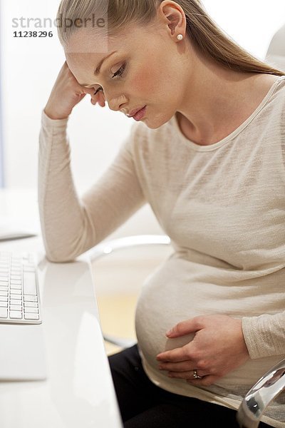 Schwangere Frau am Schreibtisch mit Kopf in den Händen