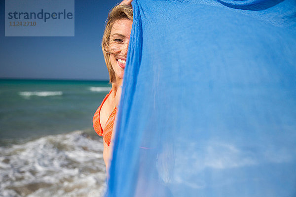 Frau hält Schal am Strand hoch