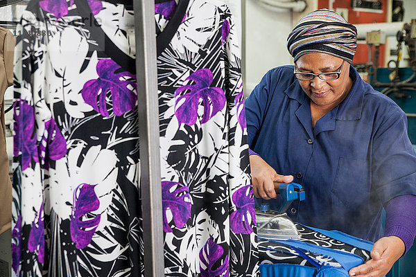 Arbeiter bügelt Kleid in Bekleidungsfabrik