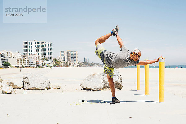 Älterer Mann  am Strand trainierend  Beinstreckung  Long Beach  Kalifornien  USA