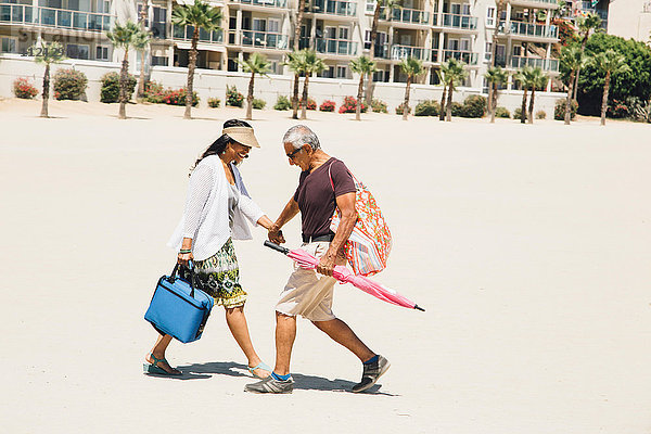 Älteres Ehepaar geht am Strand spazieren und trägt Taschen für ein Picknick  Long Beach  Kalifornien  USA