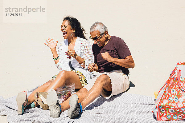 Älteres Ehepaar sitzt lachend auf einer Picknickdecke am Strand  Long Beach  Kalifornien  USA