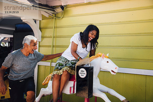 Ältere Frau beim Reiten auf einem Jahrmarkt  älterer Mann steht neben ihr und lacht  Long Beach  Kalifornien  USA