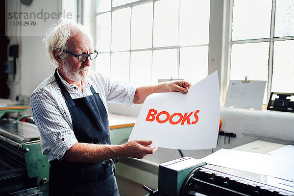 Leitender Handwerker/Techniker hält den Buchdruck in einem Buchkunst-Workshop auf