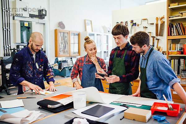 Gruppe junger Handwerker mit digitalem Tablett in einem Buchkunst-Workshop
