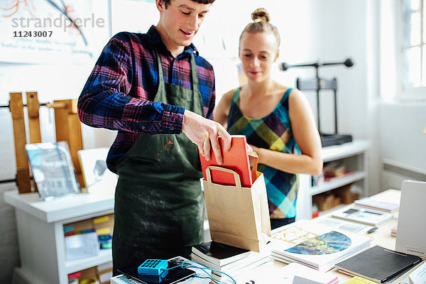 Junger Handwerker mit Kunde  der im Kunstbuchladen das Buch in die Tasche steckt