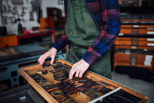 Ausschnitt eines jungen Handwerkers  der in der Druckwerkstatt durch ein Tablett mit hölzernen Hochdruckbuchstaben blickt