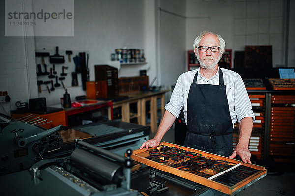 Porträt eines älteren Handwerkers neben einem Tablett mit Buchdruckbuchstaben in der Druckwerkstatt