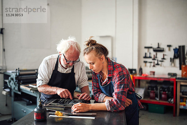 Senior-Handwerker arbeitet am Buchdruck mit einer jungen Handwerkerin in einer Druckwerkstatt
