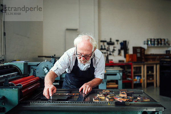 Leitender Handwerker bückt sich und benutzt Holzbuchstaben und Buchdruckmaschine in Buchkunstwerkstatt
