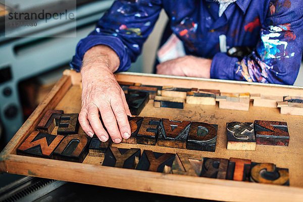 Leitender Handwerker greift nach hölzernen Buchdruckbuchstaben  Mittelteil