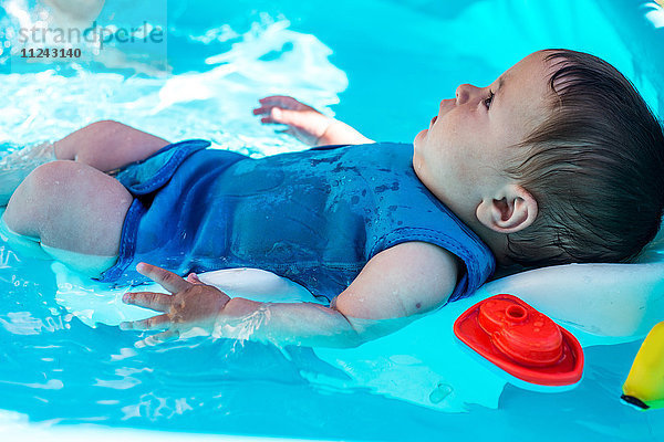 Glücklicher kleiner Junge spielt am Sommertag im aufblasbaren Schwimmbad