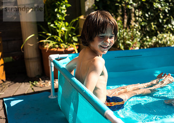Glücklicher Junge spielt am Sommertag im aufblasbaren Schwimmbad
