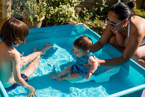 Mutter und Söhne spielen am Sommertag im aufblasbaren Schwimmbad