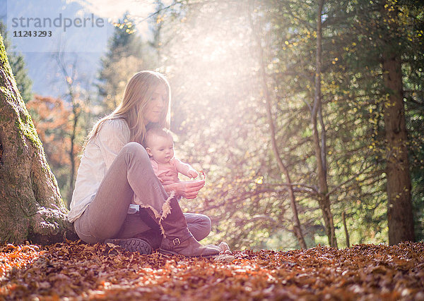 Mutter und Tochter sitzen auf dem mit Herbstlaub bedeckten Waldboden