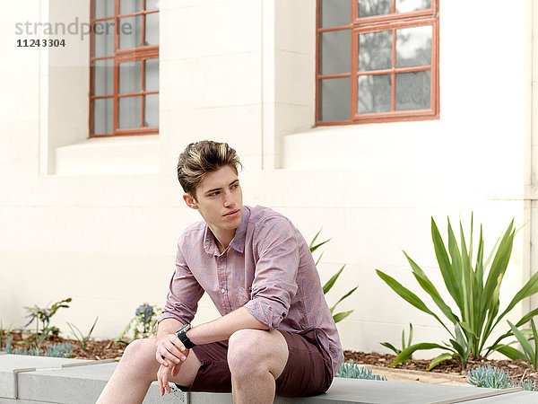 Junger Mann sitzt auf einer Stufe  im Freien  schaut weg