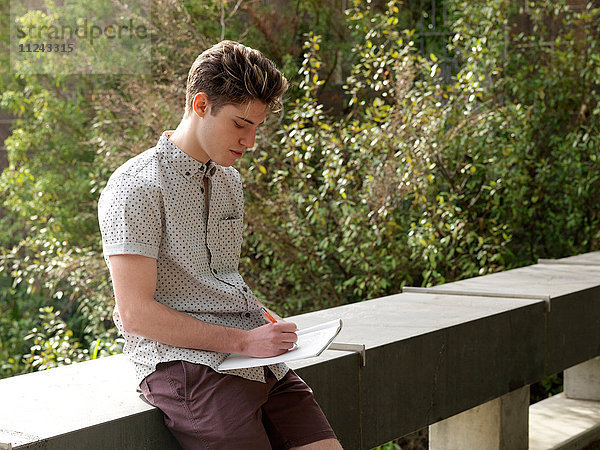 Junger Mann im Freien  schreibt Notizen auf Notizblock