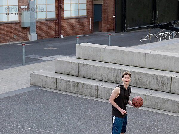 Junger Mann spielt Basketball im Freien