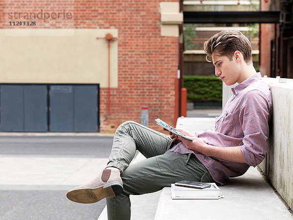 Auf Schritt und Tritt sitzender junger Mann im Freien  der ein Buch liest