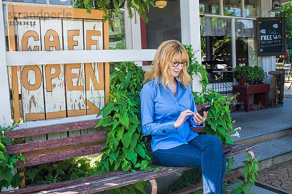 Frau benutzt Handy auf Café-Bank