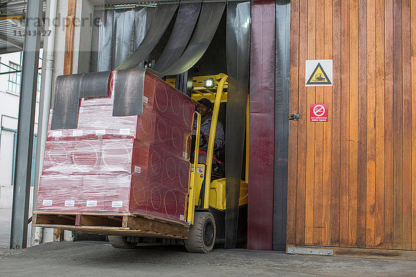 Gabelstaplerfahrer mit Paletten fährt durch die Tür einer Verpackungsfabrik