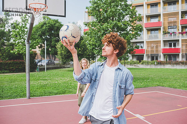 Mann balanciert Basketball  Freundin im Hintergrund