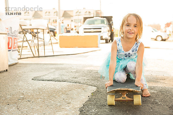 Porträt eines jungen Mädchens  das auf einem Skateboard kniet