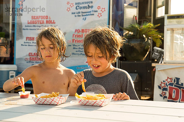 Zwei kleine Jungen essen Fastfood neben einem Fastfood-Anhänger