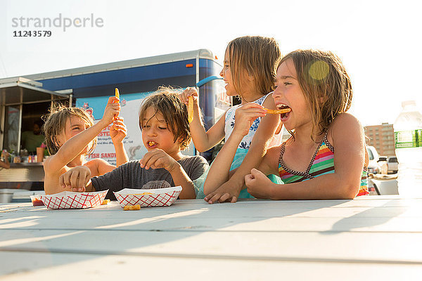 Gruppe von Kindern  die neben einem Fastfood-Anhänger Fastfood essen