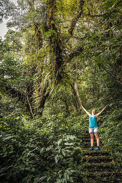 Junge Frau steht auf einer Treppe und schaut auf den Regenwald  Wana Giri  Bali  Indonesien