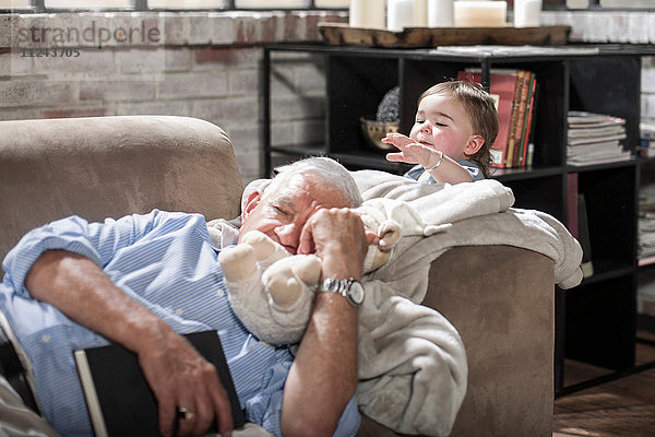 Baby Mädchen berührt schlafenden Großvater auf der Couch