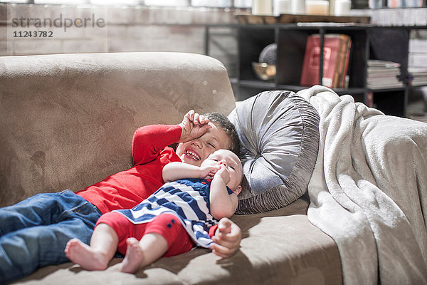 Junge und kleine Schwester liegen zu Hause auf dem Sofa.