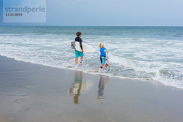Vater und Sohn stehen im Meer  halten Surfbretter in der Hand  Rückansicht