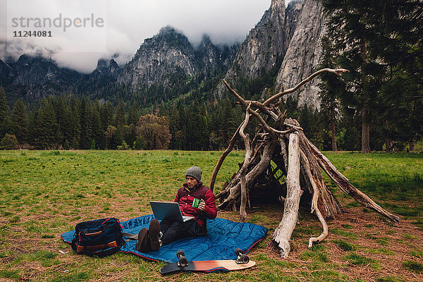 Wanderer  der mit einem Laptop an einer Höhle sitzt  Yosemite  Kalifornien  USA