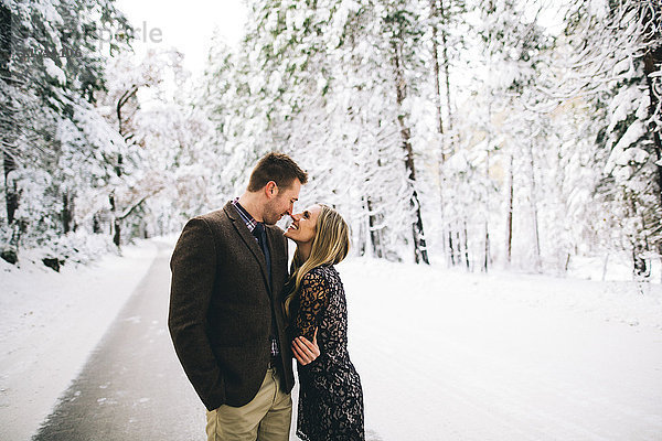 Paar in schneebedecktem Wald von Angesicht zu Angesicht lächelnd